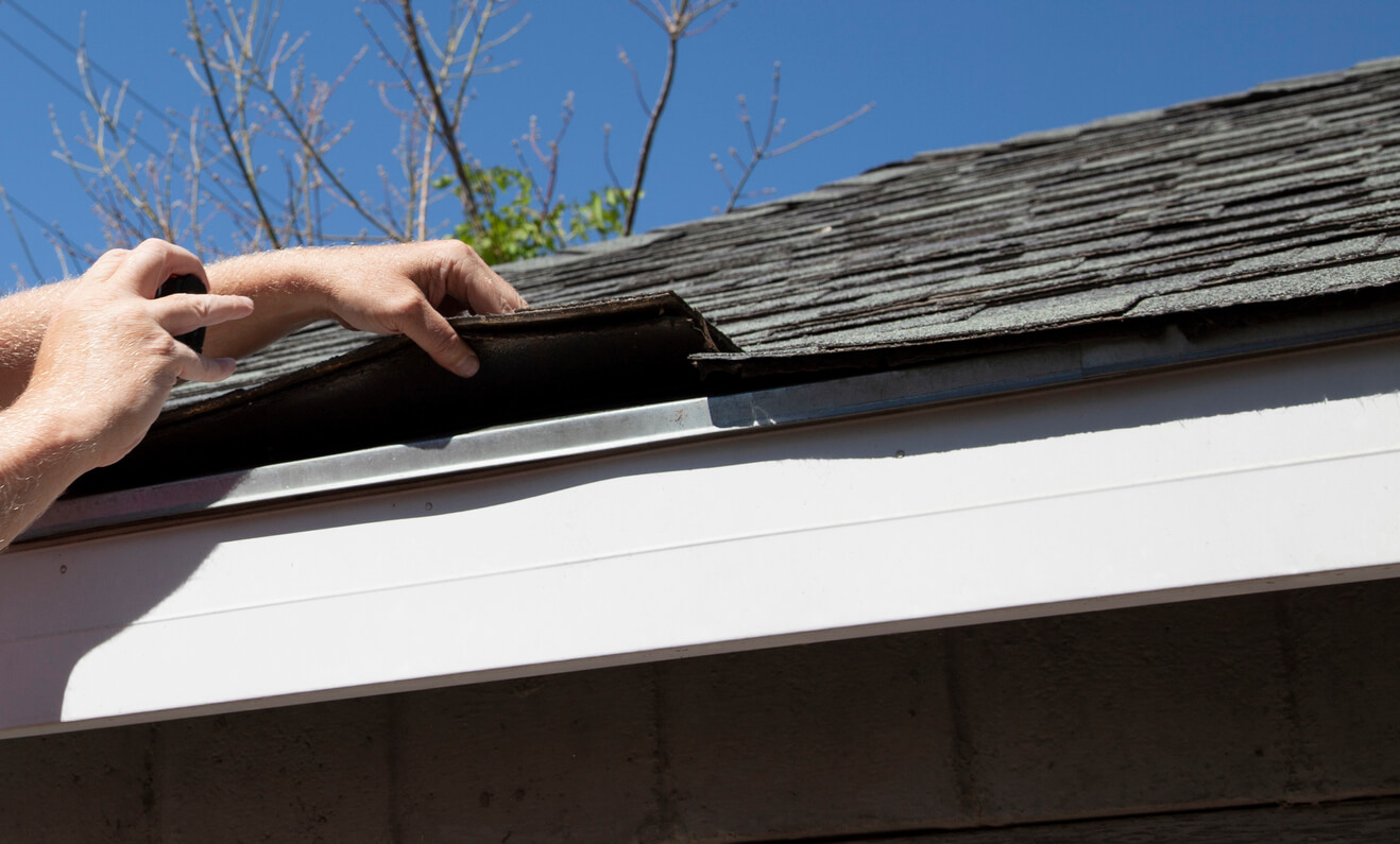 Two hands examining roof shingles